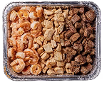 A rectangular aluminum tray contains two sections of food. The left side features cooked shrimp, while the right side has seasoned, cubed chicken. The background is a neutral tone that highlights the dish.